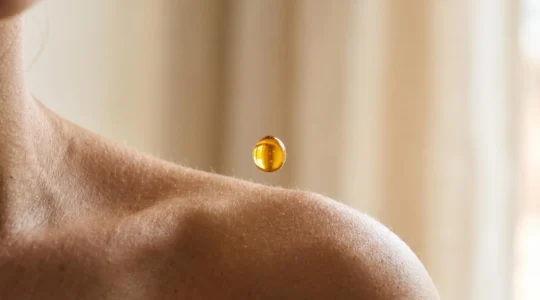 Goutte d'huile végétale dorée en suspension au-dessus d'une peau lumineuse, symbole d'équilibre entre nutrition et légèreté
